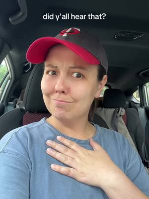 A selfie taken from inside a car. The frame is of a woman wearing a baseball cap and a blue shirt. The text overlay says, "did y'all hear that?". She appears to be reacting to something with a slight smirk, and she has her hand on her chest.