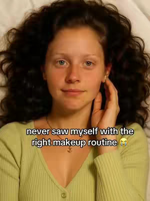 A woman, viewed from the chest up, lies on a white surface. She has long, wavy, dark brown hair and is wearing a light green v-neck sweater. She's resting her hand near her cheek with a slight smile. Text overlays the image.