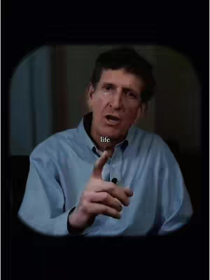 The image features a man in a light-blue button-down shirt, set against a subdued background. The man is looking directly at the camera with an apparent earnest expression. There's a text overlay in the image, positioned near the bottom. The composition uses a circular frame within a darker background, suggesting a video-like setting.