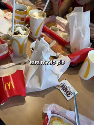 A chaotic and busy scene from either a restaurant or a home dining setting shows a table covered haphazardly with McDonald's takeout containers, drink cups with lids, and food items. The main hook text 'tara mcdo pls' is placed at the center of the image on the left edge. The composition is filled with various elements like half-eaten food and condiments. The lighting appears natural, and the close-up perspective emphasizes the clutter and immediacy of the scene.