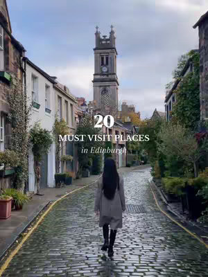 A woman walks away from the camera down a cobblestone street in Edinburgh, with buildings on either side. In the distance is a tall building with a clock tower. Text overlays, including the number "20" and the words "MUST VISIT PLACES in Edinburgh", are centered near the middle of the image.