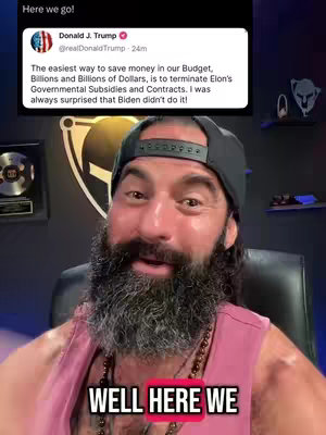 The image shows a man reacting to a screenshot of a tweet by Donald Trump. The man, who is the primary focus, is wearing a black cap and a pinkish sleeveless shirt, sitting in what appears to be an office setting with a logo behind him. The highlighted text overlay at the bottom reads "WELL HERE WE".