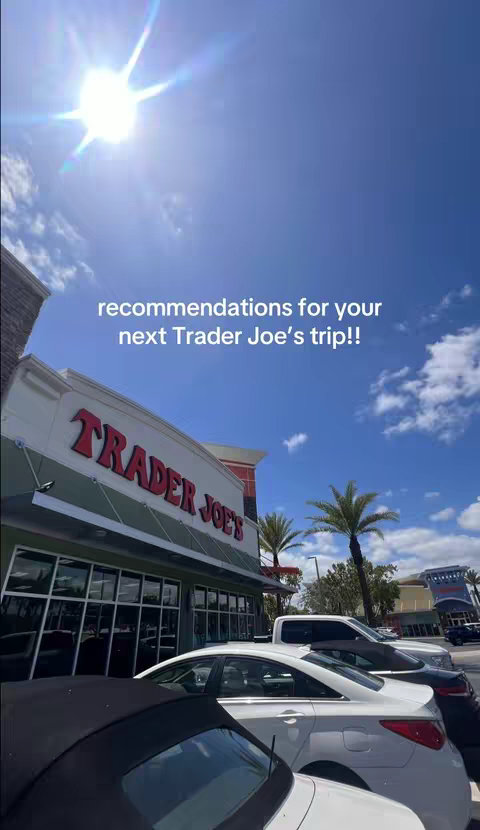 The cover image shows the exterior of a Trader Joe's store during the day. The store's sign is prominently displayed with the name 'TRADER JOE'S' in large red letters. In front of the store, several parked cars are visible, with a clear blue sky and some clouds in the background. Palm trees add to the sunny, outdoor atmosphere.