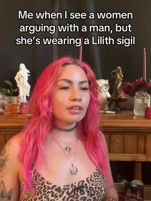 The cover image shows a woman with pink hair. Text overlay displays, "Me when I see a women arguing with a man, but she's wearing a Lilith sigil". She is wearing a leopard-print top and necklace with pendants.