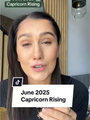 The cover image is a selfie-style shot featuring a woman positioned at the center. She is looking towards the camera with a slight smile and is in front of a light-colored wooden panel, suggesting a home or office setting. Text overlays are placed on the image; a banner stating "June 2025 Capricorn Rising" and a TikTok themed icon can be seen on the image. The overall lighting appears to be natural, with a soft, warm tone. The woman is wearing a black top and some jewerly, including a necklace.