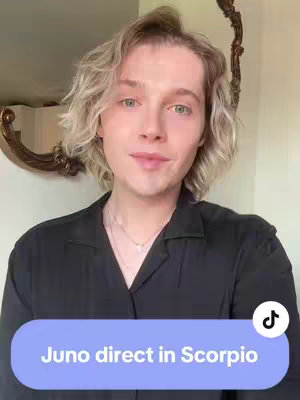 A person with light blond, wavy hair is centered in the frame. They are wearing a black button-down shirt and a delicate necklace. The background is a softly lit room with blurred elements, including a decorative mirror. Overlaying the bottom of the image is a light blue rectangle with white text.
