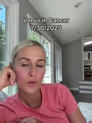 A woman with blonde hair and fair skin is looking directly at the camera with a thoughtful expression. She's wearing a red and white striped t-shirt. Behind her, a window with white framing and sunlight is visible.