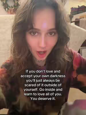 A selfie-style video cover image. A young woman with brown wavy hair and a nose piercing is centered in the frame, gazing directly at the viewer with a slightly open mouth as if speaking. She wears a colorful, tie-dye style shirt. Text overlays in a white font with black outlines are positioned at the bottom, conveying a message.