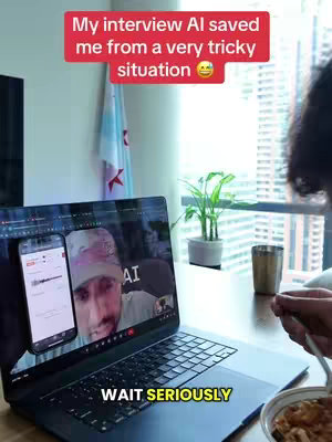 A person is sitting at a table with a laptop in front of them. The laptop screen displays a video call with a man on the screen. A phone displaying the video call is also next to the laptop.