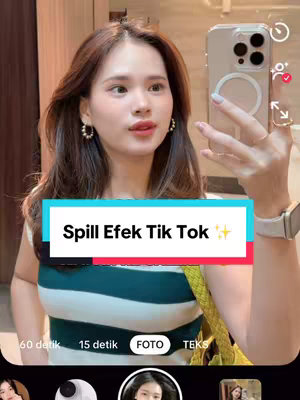 A woman takes a selfie, holding an iPhone, with a TikTok interface visible on the screen. She's in a room with wooden paneling. The phone's camera captures her face and part of her outfit, with a text overlay.