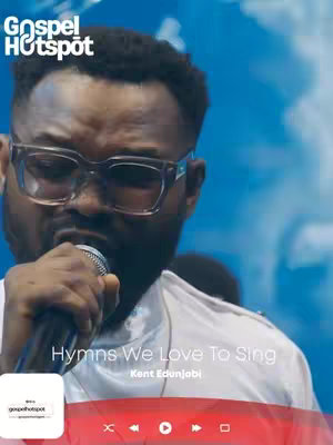 The cover image features a close-up of a Black man wearing large, square-framed glasses and holding a microphone. He appears to be singing, with his mouth open, capturing a moment of performance against a blurry blue background. Text overlays include the title of the song and the performer's name.