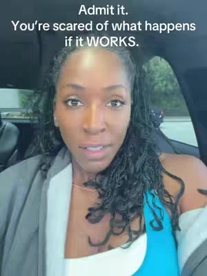 A medium shot of a woman sitting in a car, looking directly at the camera with a neutral expression. Text overlays appear at the top. The background is blurred, suggesting an out-of-focus setting.