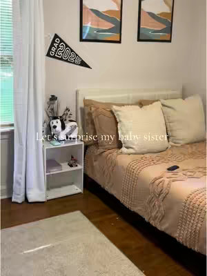 A bedroom scene with a bed, nightstand, and window. The bed has a beige comforter, and the nightstand has a small dog figure. A banner that says "GRAD 2025" hangs on the wall.