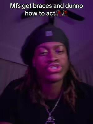 A person with long hair wearing a black beanie hat is looking at the camera with a direct gaze in a purple, studio-like environment. Text is overlayed above the person's head. The background includes a ceiling fan, and the person is wearing a black shirt and a silver chain necklace. The lighting gives a purple hue to the scene.