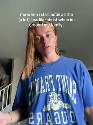 A young woman is looking towards the camera in what appears to be a well-lit space. She is wearing a blue t-shirt with white text on it. The overlay text mentions Christ and family. There is a set of stairs visible in the background.