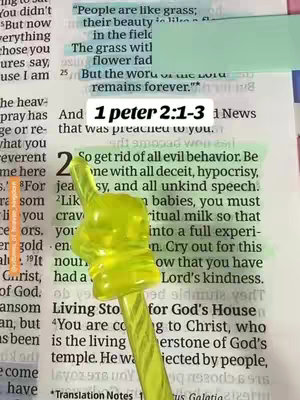 The image shows an open Bible with text highlighted in green and orange. A yellow pointer tool with a finger shaped top is placed on top of the page, pointing upwards.  The background includes other pages of the Bible with partial text and annotations.