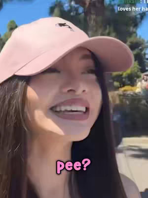 A woman with long dark hair and a pink baseball cap is smiling. A text bubble with the word "pee?" is overlaid on the image.