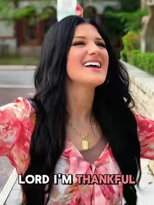 A woman with long, dark hair and a floral top smiles and looks upwards. The background is blurred, but suggests an outdoor setting with greenery. White text at the bottom says 'LORD I'M THANKFUL'.