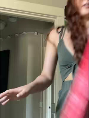 A person is shown on the side, with a green top and a reddish-pink object blocking the view. The person is captured in a doorway indoors.