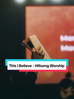 The image shows a person holding a Bible open, with their hand and the book taking up the central space. The person's arm extends upwards, and the book is angled. In the background, a red screen is visible, which appears to be a backdrop. A superimposed text overlay is present at the bottom, including the title and creator of the song. The overall lighting is dim, casting shadows and creating a sense of depth.