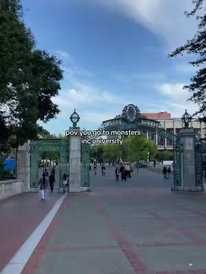 An outdoor shot of a university entrance with a grand, ornate gate. People are walking in the background, and the sky is blue.