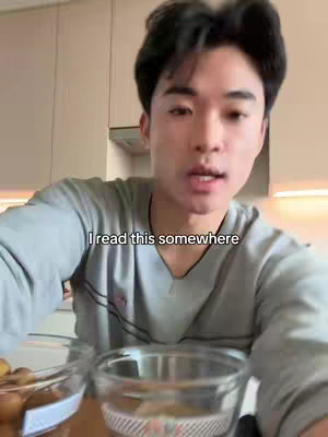 A young man is filmed from the chest up in a kitchen setting. He is wearing a grey long-sleeved shirt and speaking directly to the camera. A text overlay reads, 'I read this somewhere'.