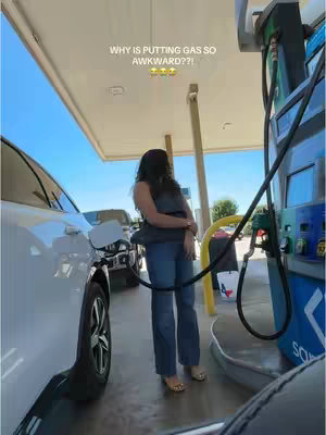 A woman stands at a gas pump, turned away from the camera, filling her car with gas. The scene takes place at a gas station with the sky visible in the background. Text overlays the top of the image.