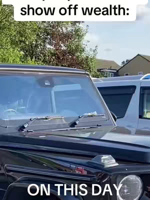 A close-up shot of a black SUV, with 'ON THIS DAY' overlaid at the bottom. In the background, there are green trees, a light blue sky, and other houses.