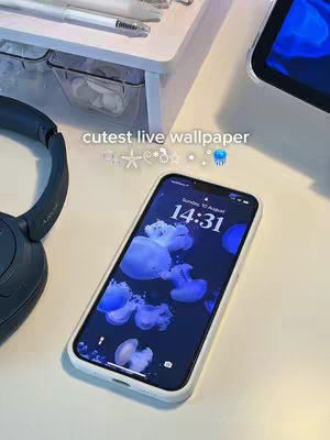 The image shows a phone displaying a custom lock screen with a jellyfish theme. The phone rests on a white surface, alongside other items. Text overlayed reads, 'cutest live wallpaper' with embellishments like stars and a jellyfish emoji.