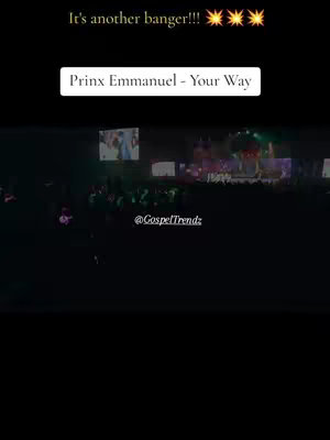 The cover image features a low-light shot of a concert or performance. The foreground is mostly dark, but a crowd of people is visible. In the background, a stage is lit up with lights. Text overlays indicate the artist, song title, and a social media handle.