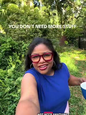 A selfie-style shot featuring a woman standing outdoors surrounded by lush greenery. The woman, with dark hair and wearing large, red-framed glasses, is smiling and looking towards the camera. She's wearing a blue top. Text overlays are present near the top and bottom, conveying the video's message. She holds a mug. The background is densely packed with trees and foliage, with a hint of a structure.