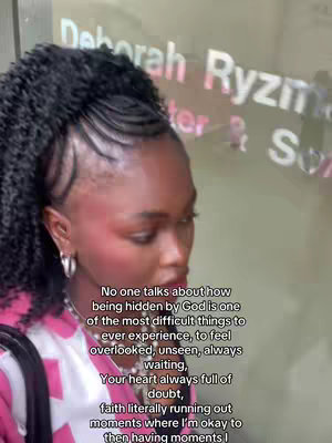 A selfie-style shot featuring a person with dark, styled hair and wearing a pink top. The person is looking slightly downwards, with a thoughtful expression. Text overlays are added to the image.