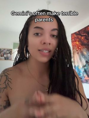 A woman with long dreadlocks and hoop earrings is centered in the frame, looking directly at the camera and speaking. overlaid text at the top of the screen. She has a tattoo on her left upper arm. The background includes a wall and a colorful tapestry.