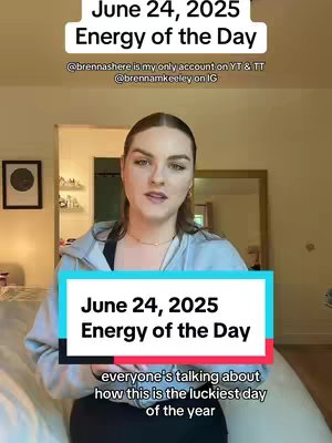 The image is a selfie-style video cover with a woman in the center, positioned against an interior background. The woman is fair-skinned with light brown hair, wearing a light blue zip-up sweatshirt and a gold necklace. A text overlay at the top reads 'June 24, 2025 Energy of the Day,' and more text is added in a lower section. Behind her, a neutral-toned room with a mirror and a picture frame is visible. The overall composition is well-lit and suggests a casual, informative video.