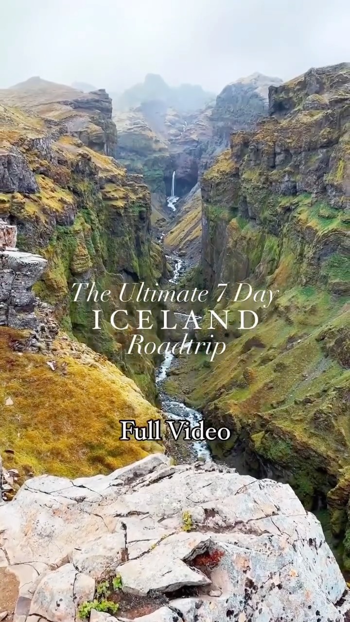 A vertical landscape image dominates the frame, showcasing a deep canyon with steep, moss-covered walls. A waterfall cascades down in the background, with a stream flowing through the canyon's center. The foreground is a rocky ledge, from which the camera appears to capture the scene. The image has muted greens and browns, suggesting a foggy or overcast day, with text overlays in white.