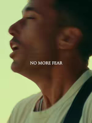 A man partially framed from the side, singing or speaking with his mouth open. The background is a soft green, and the text "NO MORE FEAR" is overlaid on the image.