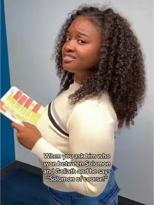 A woman with curly dark hair is on the left side, wearing a cream sweater and jeans. She is holding a book and looking to the right with a questioning expression, one eyebrow raised. Text overlay is set below.