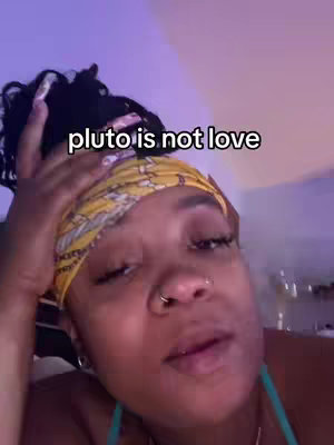 A close-up shot of a person with a yellow bandana on their head, the text overlayed on the image reads "pluto is not love".
