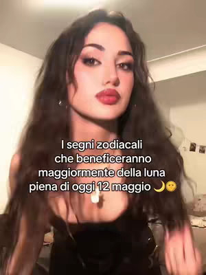 A medium shot shows a young woman with long, wavy brown hair looking directly at the camera. She has full, red lips and is wearing makeup. Overlayed text in white describes zodiac signs and the full moon. The background is blurred, suggesting an indoor setting.