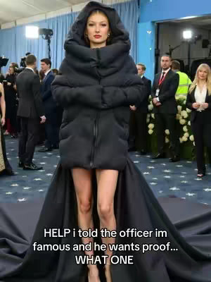 A woman is standing on a black carpet wearing a large, black, hooded coat and a short skirt, with an outdoor event in the background. The text overlayed on the image says, "HELP i told the officer im famous and he wants proof... WHAT ONE".