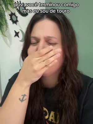 A woman with long, dark hair covers her mouth with her hand, eyes closed. The background is a soft green color and there are decorative objects behind her.