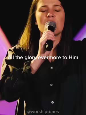 A woman is singing into a microphone with her eyes closed, likely in a performance setting. Text overlay displays part of a worship song. The background seems to be a stage.