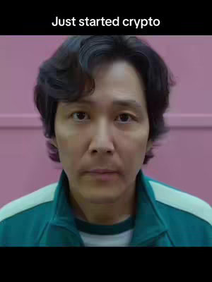 A medium shot features a man facing the camera with a neutral expression. He wears a dark green jacket with white accents and the background is a consistent pink color. Text overlayed at the top says, 'Just started crypto'.
