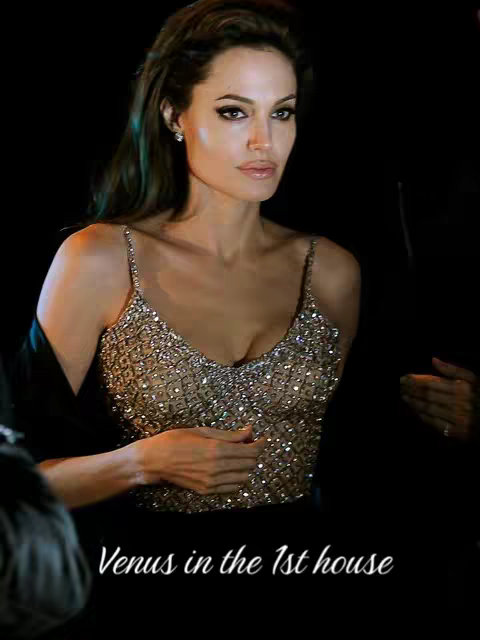 The image features a close-up of Angelina Jolie, with her face centered, and a dark background. She is looking slightly to the side, with soft lighting highlighting her features. The text overlay at the bottom, 'Venus in the 1st house', written in a stylish script, adds context to astrological themes.