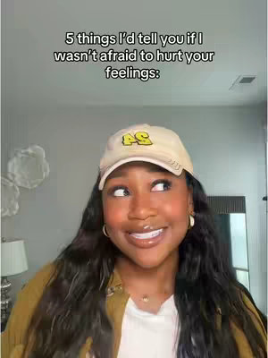 A woman with long, dark hair is looking slightly to her right with a soft smile. She is wearing a baseball cap, a collared jacket, and a white shirt. The background is a neutral, light-colored wall with a few decorative elements.