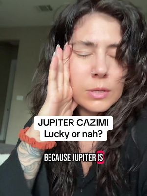 A well-lit selfie shows a woman with dark, curly hair. She wears a black top and a red bracelet. Her eyes are closed, and she has her right hand to her face near her forehead. Text overlays include, "JUPITER CAZIMI Lucky or nah?" and "BECAUSE JUPITER IS". The background is a soft-focus interior.