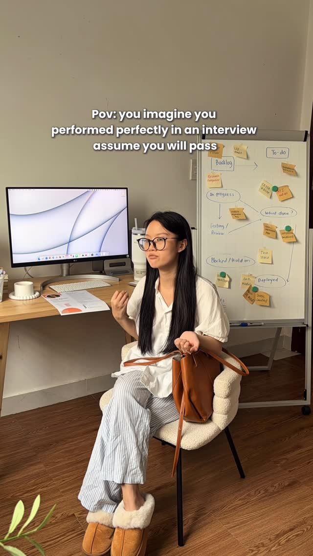 A young woman wearing glasses, white shirt and striped pants is sitting in a chair in front of a desk with a computer. She is in a well-lit room, with wooden floors and neutral-colored walls. On a whiteboard behind her are notes and diagrams. Text overlay indicates this is a relatable moment about interviews.