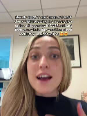 A selfie-style video shows a young woman talking directly to the camera; text overlay on the video. The woman is centered in the frame, with her face and upper body visible. She has long, blonde hair and is wearing a dark top. The background is a plain office setting, with a hint of items like a framed picture. The lighting appears to be natural, and the focus is on the woman's expression.
