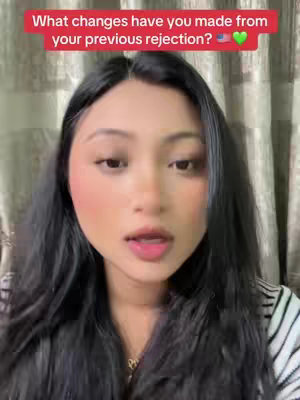 A woman with long black hair and fair skin is the focus. She is looking directly at the camera with a slightly open mouth, possibly speaking. Her cheeks have a touch of blush, and she wears light makeup. A text overlay appears at the top in a red box, asking a question. The background is a soft, neutral color curtain.