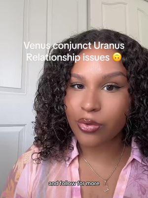A woman with curly dark hair is centered, her face is the main focus. Text overlays the image, and below her, there's a blurred background. She wears a pink, floral-patterned shirt and a delicate necklace with a pendant. The composition is well-lit, highlighting her features and the text.